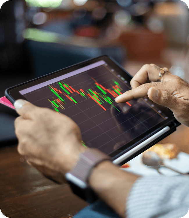 Hand interacting with a tablet showing a candlestick chart